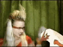 a woman wearing glasses and a mohawk stands next to a stuffed animal