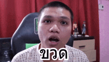 a man with a shaved head is sitting in a chair with his mouth open and a foreign language written on his face .