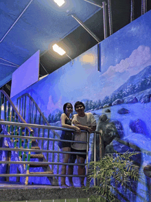 a man and a woman are posing for a picture in front of a waterfall painting