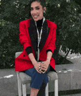 a woman in a red jacket is sitting on a chair with her legs crossed