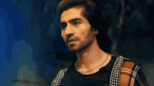 a man with a mustache is wearing a plaid shirt and a black shirt and looking at the camera .