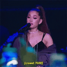 ariana grande is singing into a microphone on a stage and talking to the crowd .