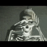 a skeleton is covering his face with his hands in a dark room .