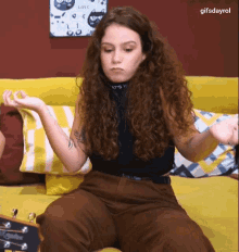 a woman with curly hair is sitting on a yellow couch with a guitar in front of her