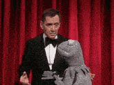 a man in a tuxedo holds a glove over a frog