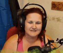 a woman wearing headphones and a pink shirt is sitting in front of a microphone .