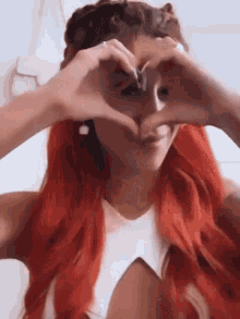 a woman with red hair making a heart with her hands