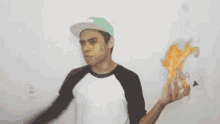 a young man wearing a hat is holding a torch in front of a white wall .