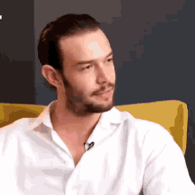 a man with a beard is sitting in a yellow chair wearing a white shirt and smiling .