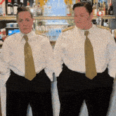 two women wearing white shirts and gold ties are standing in front of a bar