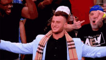 a man wearing a plaid scarf and a blue jacket is standing in front of a crowd .
