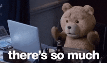 a teddy bear is sitting at a table with a laptop and a bottle of beer .