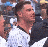 a man in a striped baseball uniform is sitting in a stadium with other people .
