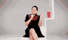 a woman in a black dress is sitting on the floor with her legs crossed while looking at her phone .