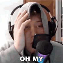 a person wearing headphones and a hoodie is holding a cell phone in front of a microphone and says oh my