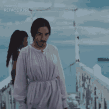 a man in a white robe is standing on a bridge with a woman behind him