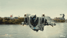 a robot is flying over a body of water with a disney logo in the corner