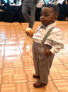 a little boy wearing suspenders and a bow tie holds a bread roll