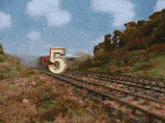 a train going down the tracks with the number 5 in the foreground