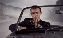 a man in a suit and tie is driving a car and holding a fork in his hand .
