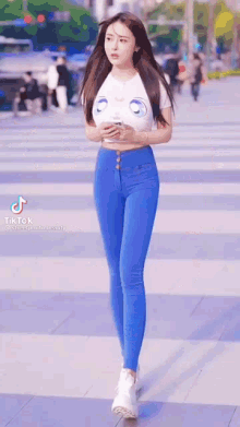 a woman wearing blue jeans and a white crop top is walking down the street .