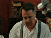 a man wearing suspenders and a white shirt is looking down