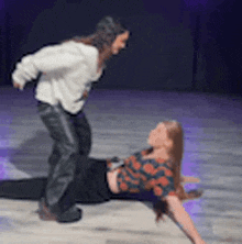 a woman is laying on the floor while a man is standing next to her .