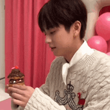 a young man in a sweater is holding an ice cream cone with a cupcake on it .