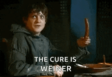 a man is sitting at a table holding a sausage and a bowl of soup .