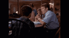 a man in a blue shirt is sitting at a table talking to a boy