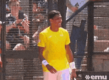 a man in a yellow shirt is holding a tennis racquet in front of a emu sign