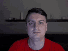 a man in a red shirt looks at the camera in a dark room