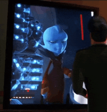 a man is standing in front of a tv screen with a blue alien on it
