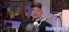 a man wearing a hat is sitting in front of a microphone with the words dark web on the bottom right .