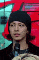 a young man wearing a black hat is talking into a microphone .