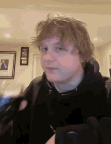 a young man with blonde hair is wearing a black hoodie and holding a cell phone .
