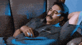 a man with a mustache is laying on a couch with his hands behind his head
