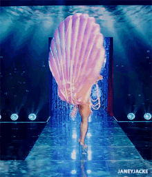 a woman in a seashell costume is walking down a runway with the words janeyjacke below her