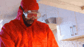 a man wearing a red suit and goggles stands in a kitchen