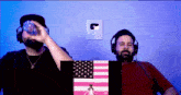 two men wearing headphones are sitting in front of a pink flag