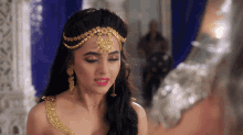 a woman wearing a gold headpiece and earrings looks at something