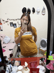 a woman taking a selfie in front of a mirror wearing a t-shirt that says coow2