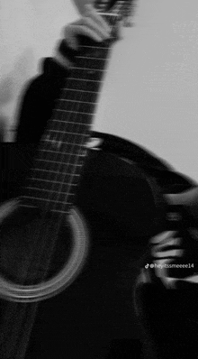 a black and white photo of a person holding an acoustic guitar .