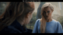 a woman in a blue sweater is looking at another woman in a black coat .