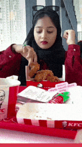 a woman in a hijab is eating fried chicken from a kfc tray