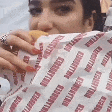 a woman is eating a hamburger wrapped in a paper that says billabong .