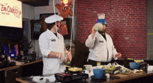 two men are cooking in a kitchen and one has the word chad on his jacket