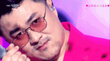 a close up of a man wearing glasses and a pink shirt that says live on it