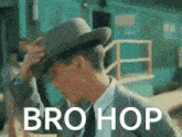a man in a suit adjusts his hat with the words bro hop above him