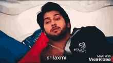 a man with a beard is laying on a bed with the name srilaxmi on the bottom of the screen